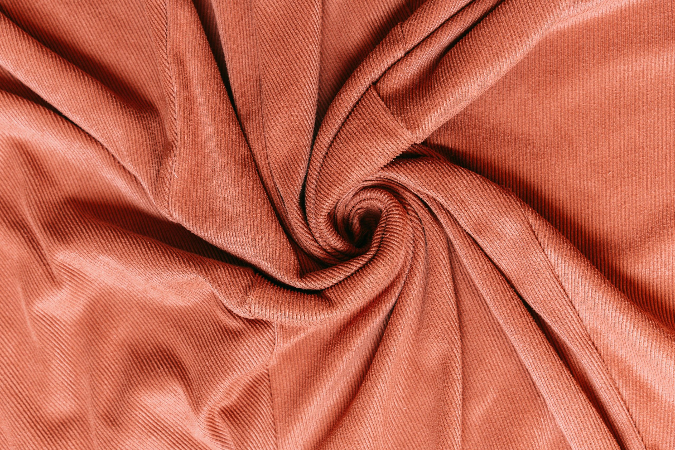 Richly textured corduroy fabric arranged in a spiral, showcasing its detailed pattern and warm color.
