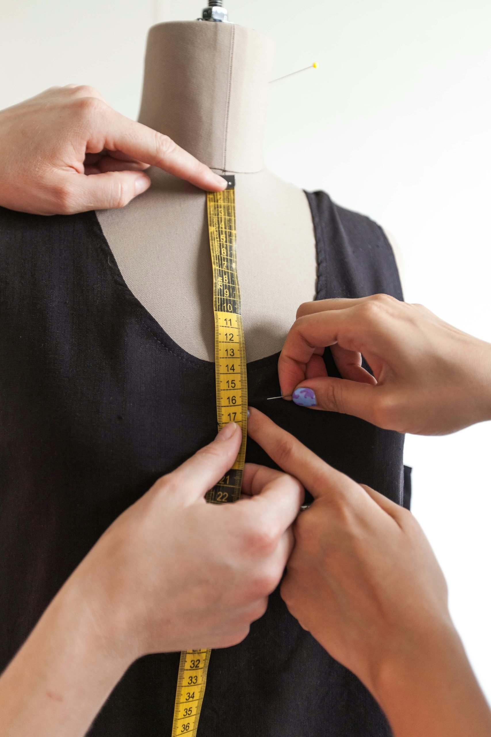 Home Close-up of hands using a tape measure on a mannequin wearing a black dress. Fashion concept.